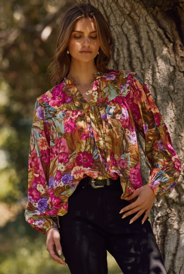 Woman wearing a colorful floral blouse standing against a tree