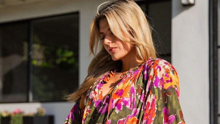 Woman wearing a colorful floral dress sitting outdoors.